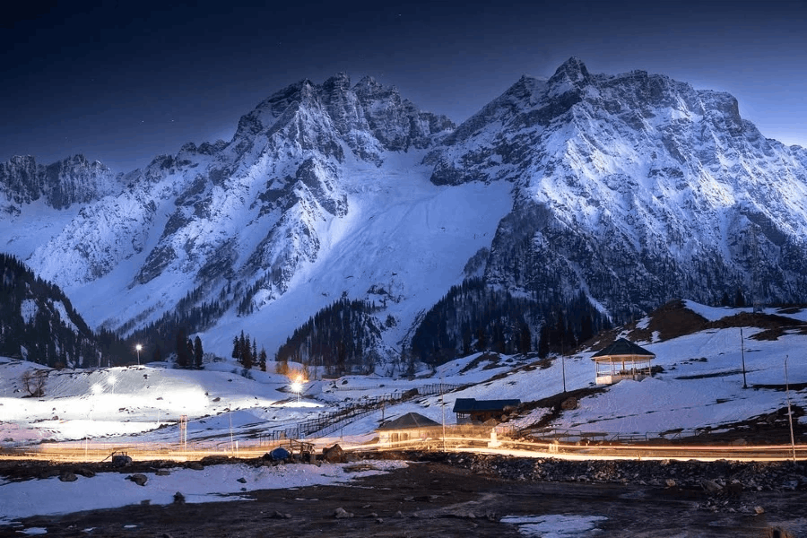 Snow-covered Sonamarg mountains near Sindh Resorts with a scenic night view, river, and illuminated road.