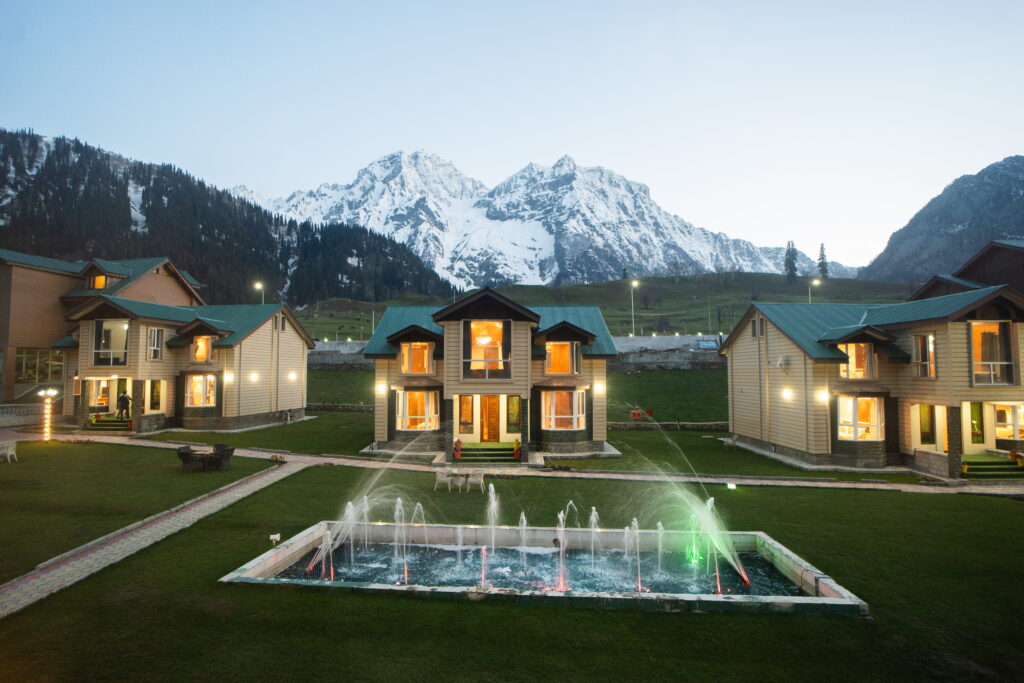 Sindh Resorts luxury cottages in Sonamarg, Kashmir with mountain views, landscaped garden, and illuminated fountain.