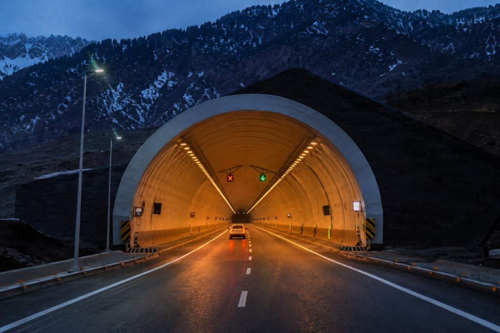 Vehicle entering Sonamarg Tunnel at night with illuminated roadway and mountain backdrop
